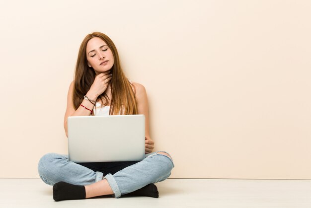 Young ginger woman sitting on her house floor suffers pain in throat due a virus or infection.