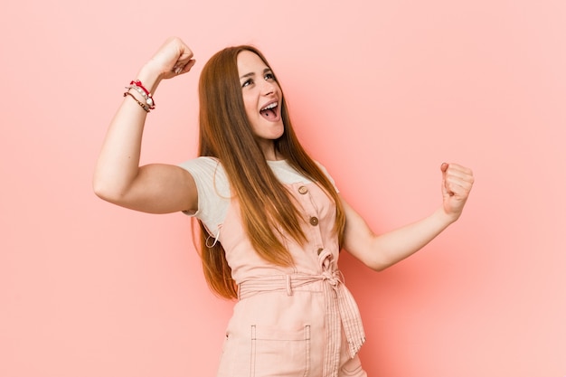 Young ginger woman with freckles raising fist after a victory, winner concept.