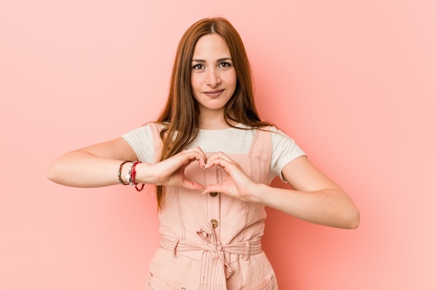 Фото Молодая женщина имбиря с веснушками усмехаясь и показывая форму сердца с руками.