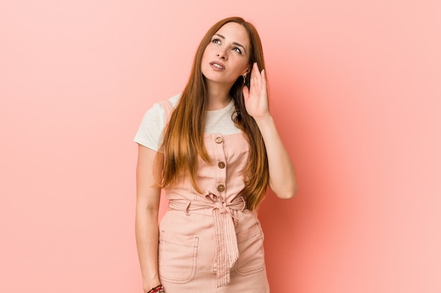 Young ginger woman with freckles trying to listening a gossip.