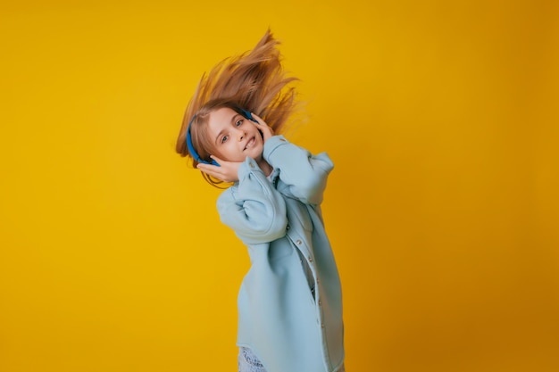 A young girl 1113 years old in headphones listens to music and dances in the studio on a yellow background