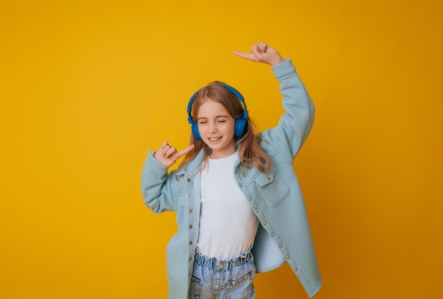 A young girl 1113 years old in headphones listens to music and dances in the studio on a yellow background