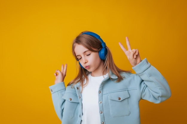 A young girl 1113 years old in headphones listens to music and dances in the studio on a yellow background