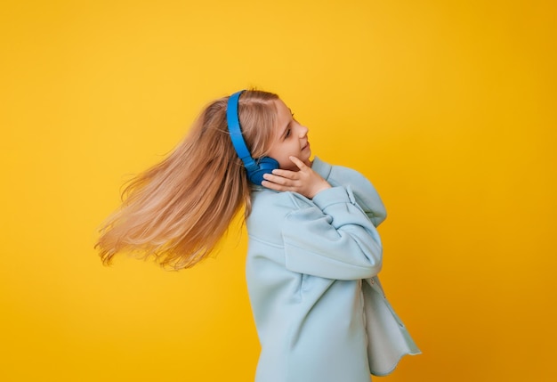 A young girl 1113 years old in headphones listens to music and dances in the studio on a yellow background