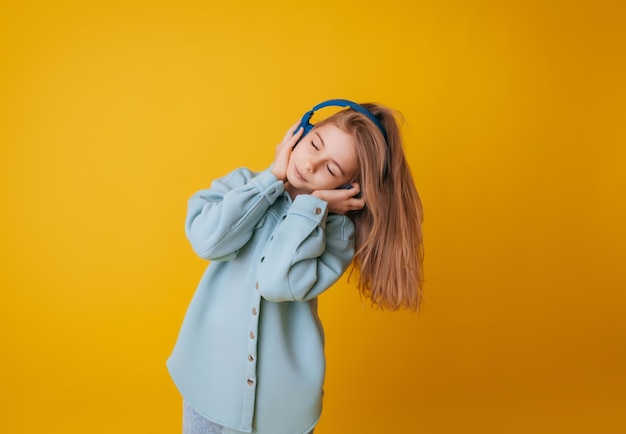 A young girl 1113 years old in headphones listens to music and dances in the studio on a yellow background