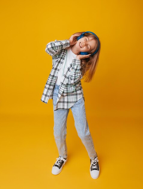 A young girl 1113 years old in headphones listens to music and dances in the studio on a yellow background