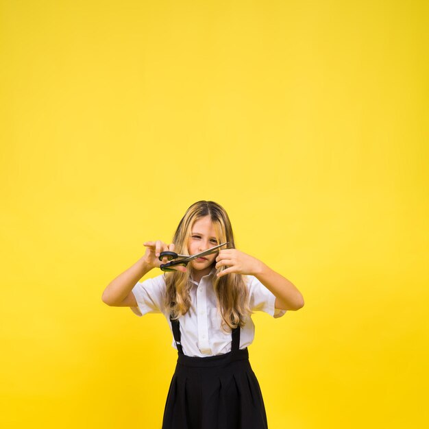 A young girl about to cut her own hair with a pair of scissors isolated against yellow background