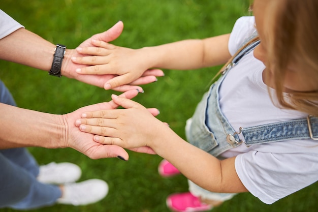 Young girl and adult woman taking their hands together while standing on the green grass