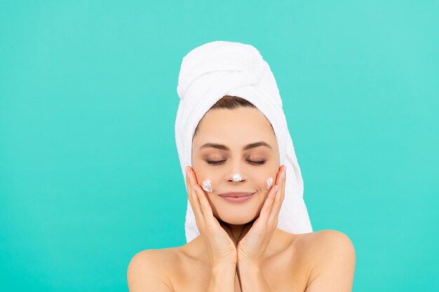 Young girl apply face cream on blue background