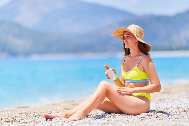 Young girl applying sunscreen lotion while sunbathing and relaxing on beach by the sea in sunny summer day Sun protection