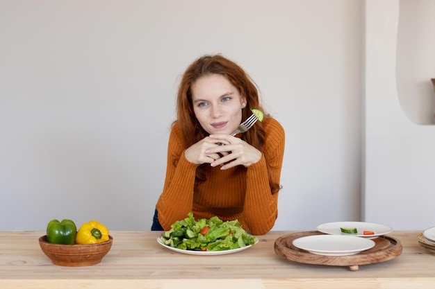 Young girl in an apron makes a healthy salad of vegetables and herbs in her kitchen