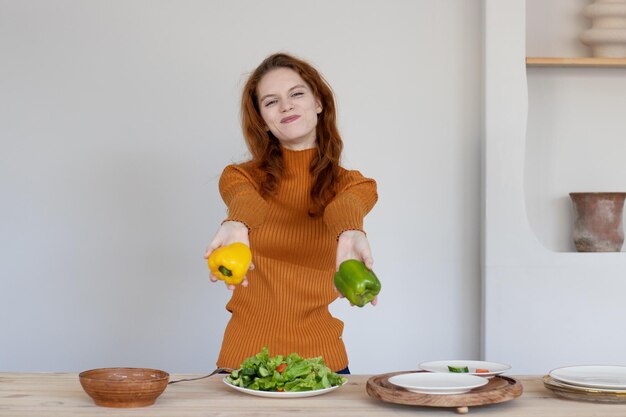 エプロンの少女は、キッチンで野菜とハーブのヘルシーなサラダを作ります