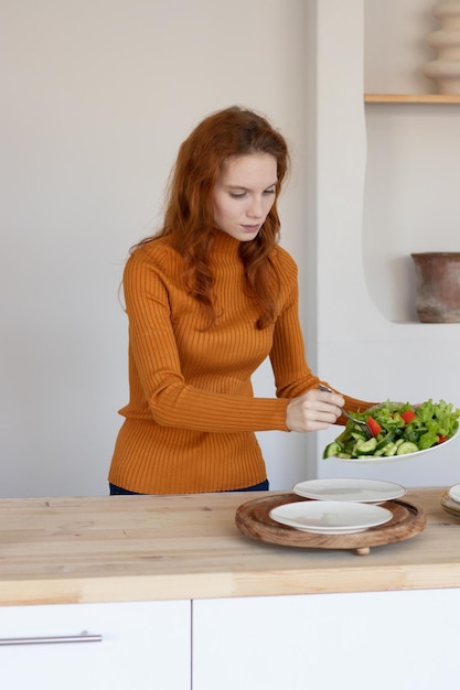 Photo young girl in an apron makes a healthy salad of vegetables and herbs in her kitchen