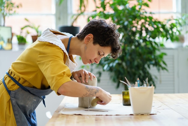 사진 스튜디오에서 도자기 수업이나 워크샵을 하는 동안 원시 점토로 주전자를 모델링하느라 바쁜 어린 소녀 장인