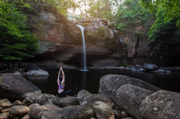 Le donne asiatiche della ragazza sta giocando lo yoga davanti alla cascata