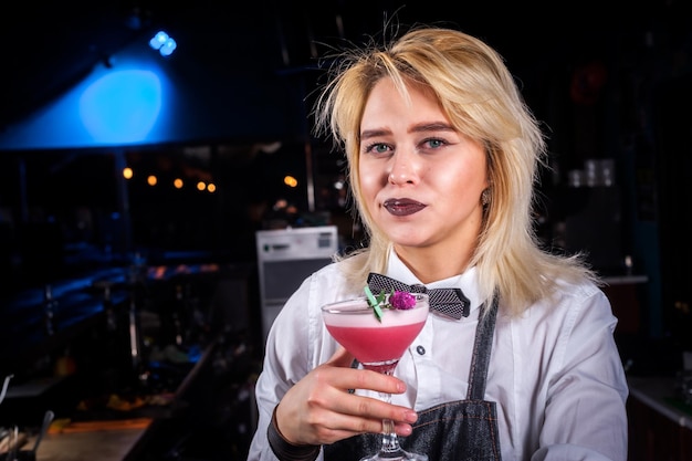 Young girl barman creates a cocktail while standing near the bar counter in pub