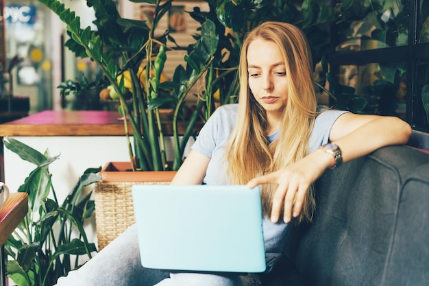 Молодая блондинка-менеджер в уютном кабинете на диване с ноутбуком поколения тысячелетий