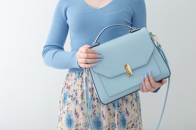 Young girl in blue blouse and pleated skirt with blue handbag on white background