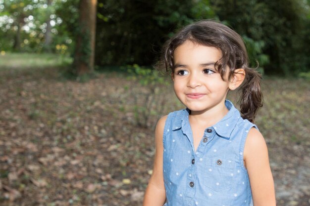 Young girl in blue dress standing in a summer park looking side