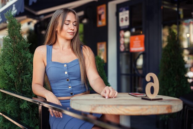 A young girl in a blue top in a cafe at the table looks away