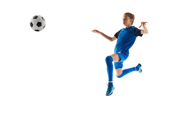 青いユニフォームを着た若い女の子サッカー選手が白い色に隔離された動きでボールをる練習をしています