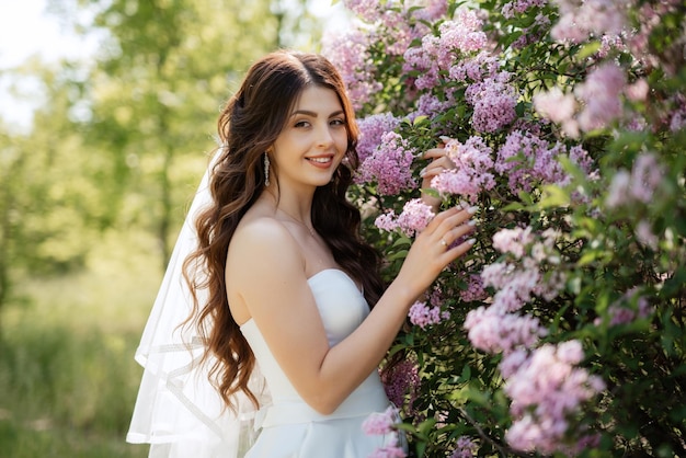 Young girl bride in a white dress in a spring forest in lilac bushes