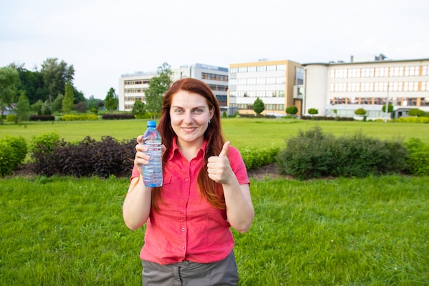 Young girl in bright summer clothes holds a plastic bottle of water 