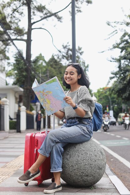여행 목적지를 찾고 지도를 읽는 동안 어린 소녀는 길가에 앉아 가방을 가져