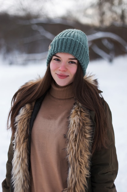 冬の風景を背景に、セーター、帽子、緑のジャケットを着たブルネットの少女。雪と霜、クリスマスのコンセプト。