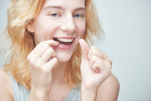Молодая девушка чистит зубы зубной нитью, крупным планом на белом фоне