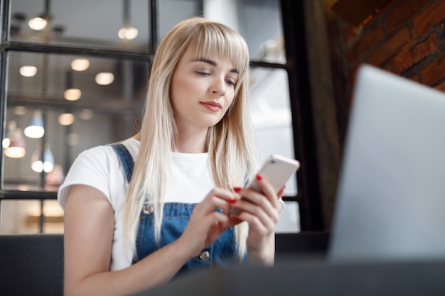 コーヒーを飲みながら携帯電話を使用してカフェで若い女の子。オンラインショッピング