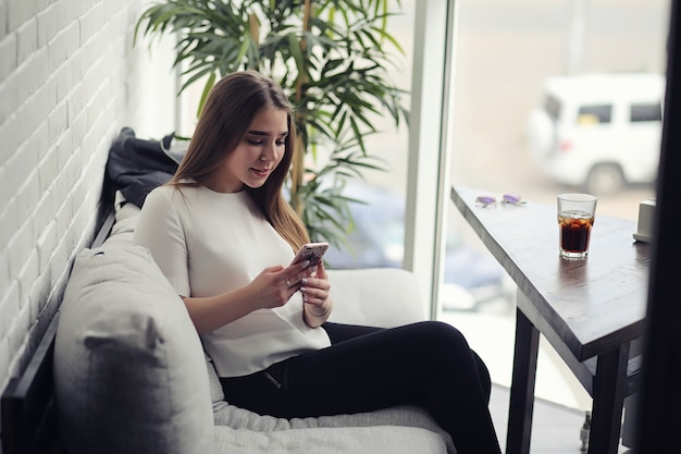 Young girl in a cafe. The girl is sitting on the couch and talking on the phone.