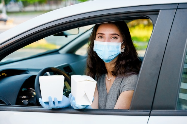 Young girl in car in medical gloves and mask holds wok in box