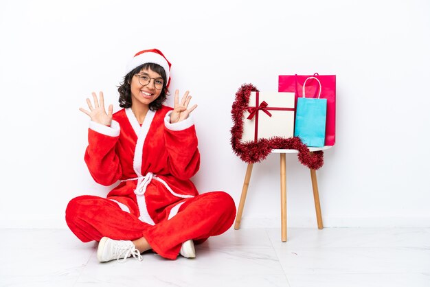 Young girl celebrating Christmas sitting on the floor isolated on white bakcground counting nine with fingers