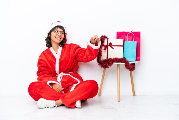 Young girl celebrating Christmas sitting on the floor isolated on white bakcground giving a thumbs up gesture