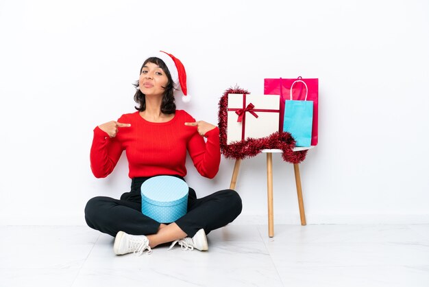 Young girl celebrating Christmas sitting on the floor isolated on white bakcground proud and self-satisfied