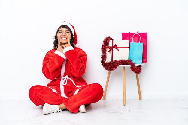 Young girl celebrating Christmas sitting on the floor isolated on white bakcground smiling with a happy and pleasant expression