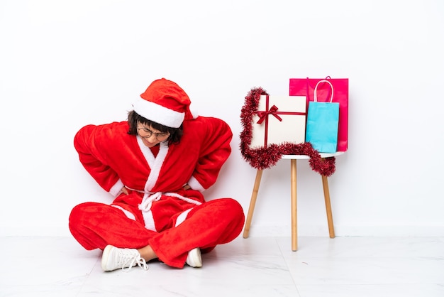 Giovane ragazza che celebra il natale seduta sul pavimento isolato su sfondo bianco che soffre di mal di schiena per aver fatto uno sforzo