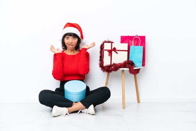 Young girl celebrating Christmas sitting on the floor isolated on white bakcground with shocked facial expression