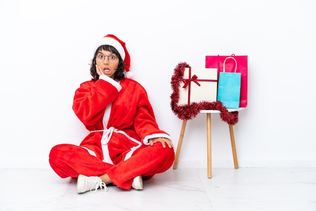 Young girl celebrating Christmas sitting on the floor isolated on white bakcground with surprise and shocked facial expression