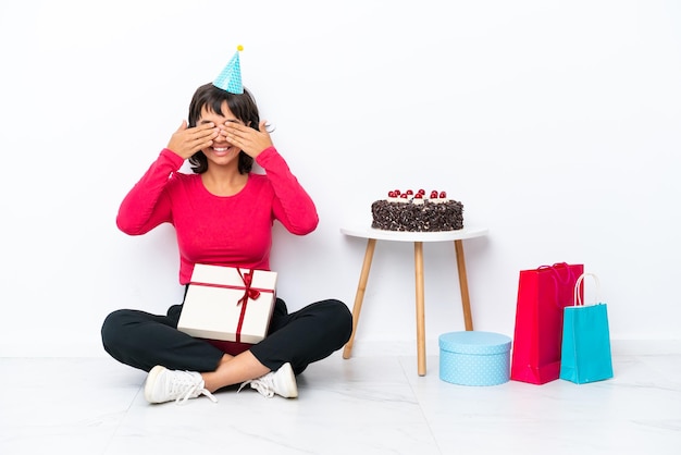 手で目を覆っている白い背景で隔離の床に座って彼の誕生日を祝う少女