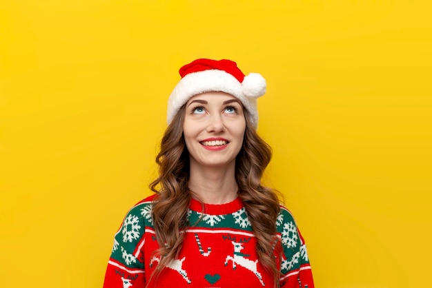 young girl in christmas sweater and santa claus hat smiles and looks up at copy space