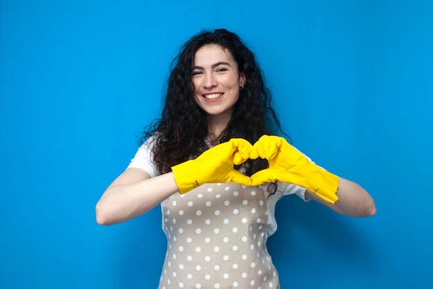 young girl cleaner in uniform and gloves for cleaning shows heart with her hands and smiles