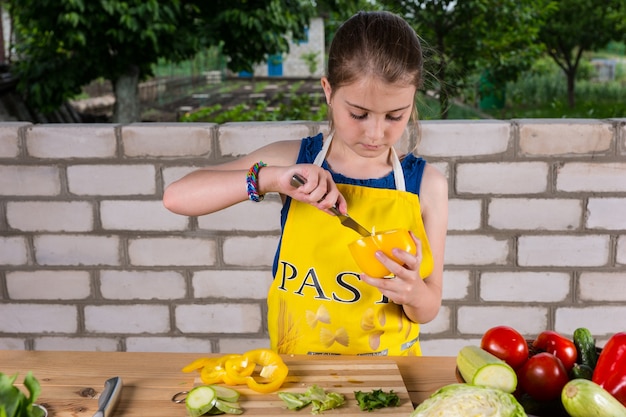 Young girl cleaning out a sweet pepper removing the pith with a paring knife as she prepares an assortment of fresh vegetables