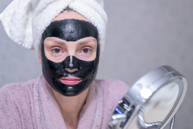 Young girl in a cleansing black coal mask on her face.