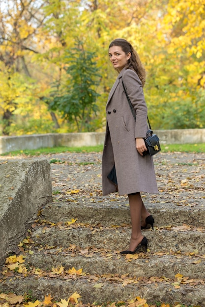 A young girl in a coat poses in a park on a background of golden autumn foliage.