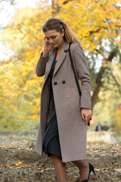 A young girl in a coat poses in a park on a background of golden autumn foliage.