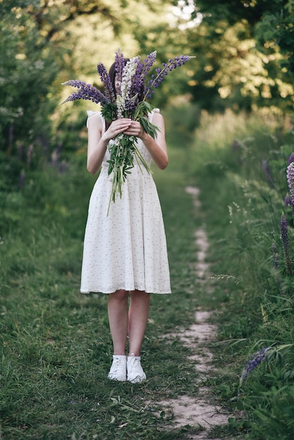 緑豊かな公園で暖かい春に若い女の子がルピナスの花で顔を覆います