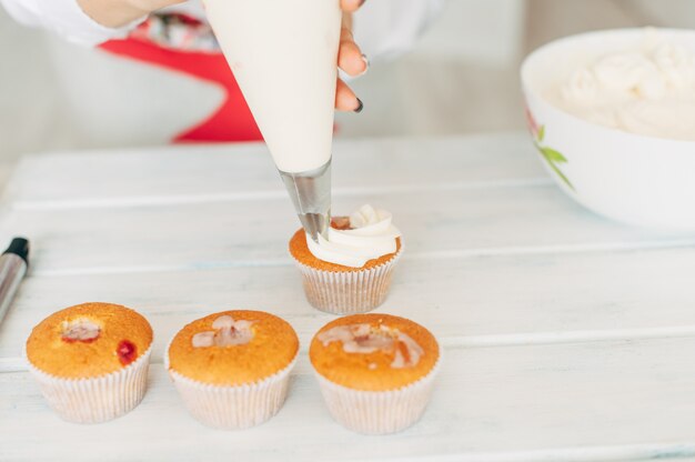 A young girl decorates cupcakes with cream. 