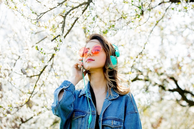 Young girl in a denim jacket and headphones near a flowering tree in the park. Spring season